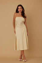 Model standing front-facing in beige strapless midi dress with floral embroidery at bodice
