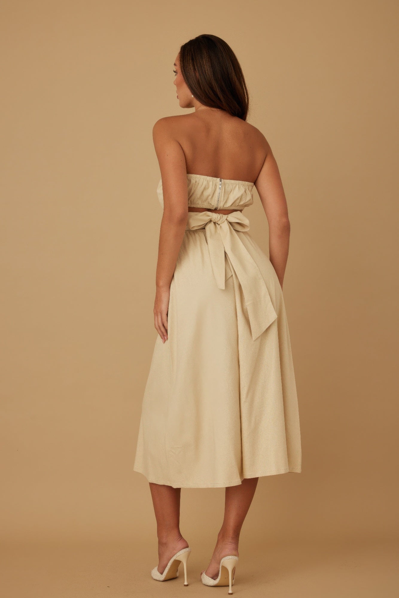 Back view of beige strapless midi dress featuring smocked top and tie-back bow detail
