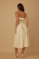 Back view of beige strapless midi dress featuring smocked top and tie-back bow detail
