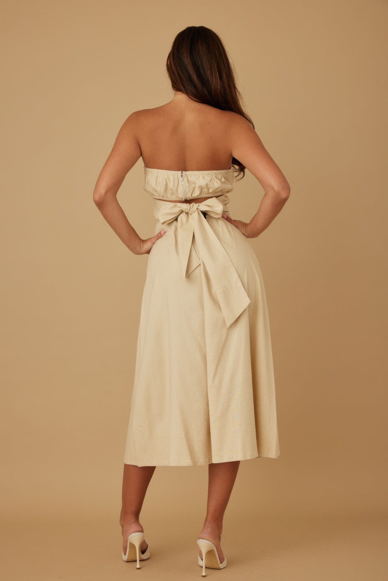 Back view of beige strapless midi dress featuring smocked top and tie-back bow detail
