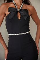 Detail shot of the black jumpsuit highlighting the satin bow, rhinestone halter straps, and rhinestone waist trim.