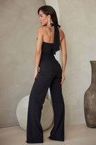 Full back view of black wide-leg halter jumpsuit, featuring neck ties and a fitted bodice, photographed in a neutral room.
