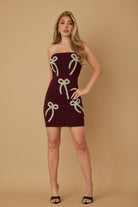 Burgundy strapless mini dress with pearl and stud bow embellishments, front view on model.