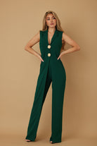 Emerald green jumpsuit featuring deep V neckline and gold shank buttons, hands on waist
