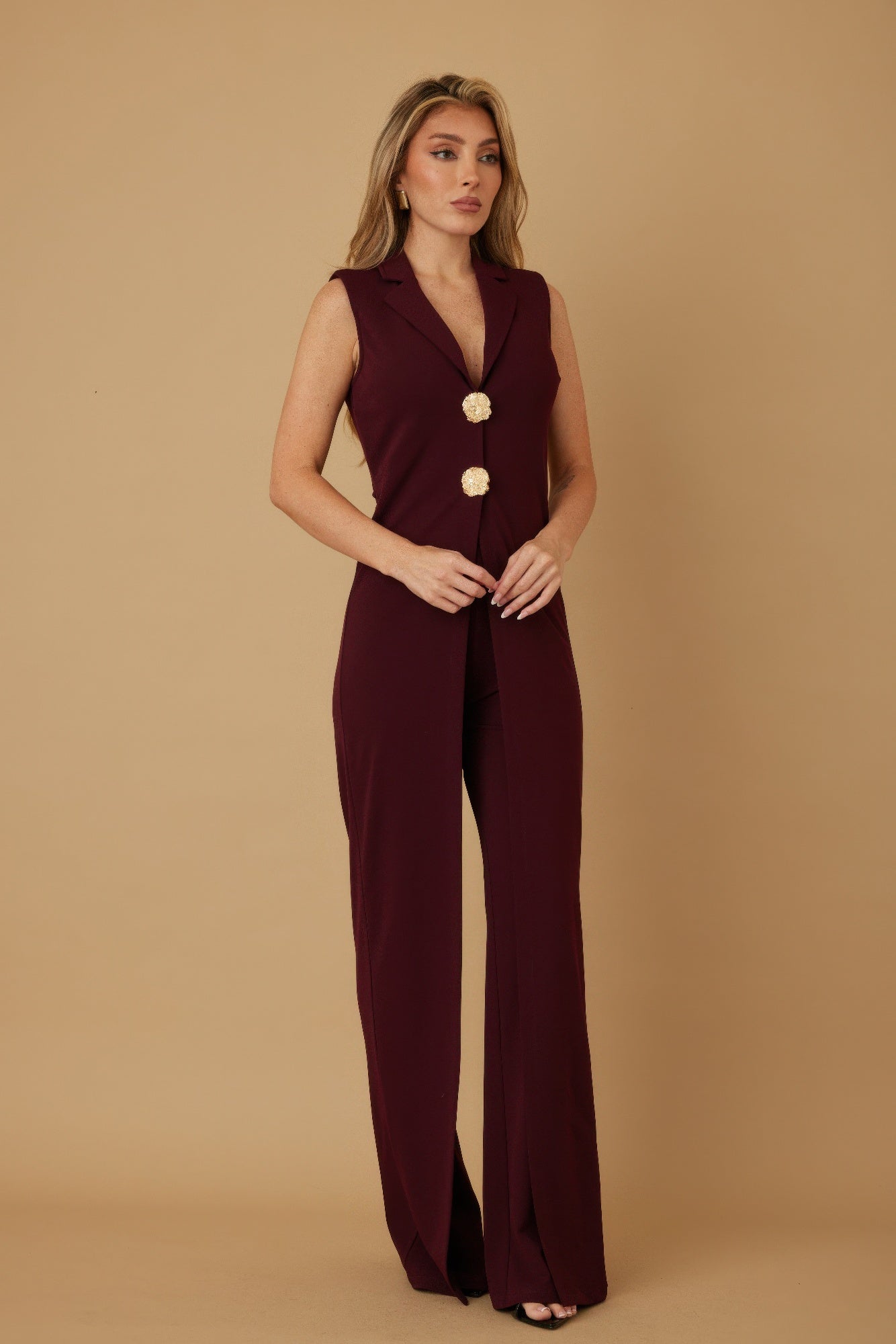 Three quarter view of burgundy wide leg jumpsuit showing deep V lapel and gold button detail, AVAH
