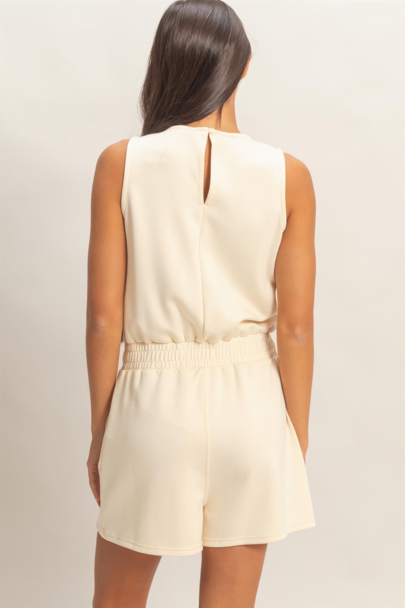 Back view of cream sleeveless romper with elastic waist and keyhole closure
