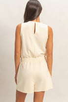 Back view of cream sleeveless romper with elastic waist and keyhole closure
