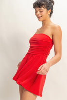 Side view of red strapless romper with ruched waist and flowy skirt