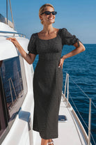 Model wearing the Cala Luna Puff Sleeve Midi Dress in black polka dot while standing on a yacht, featuring a scoop neckline, puff sleeves, and midi length.