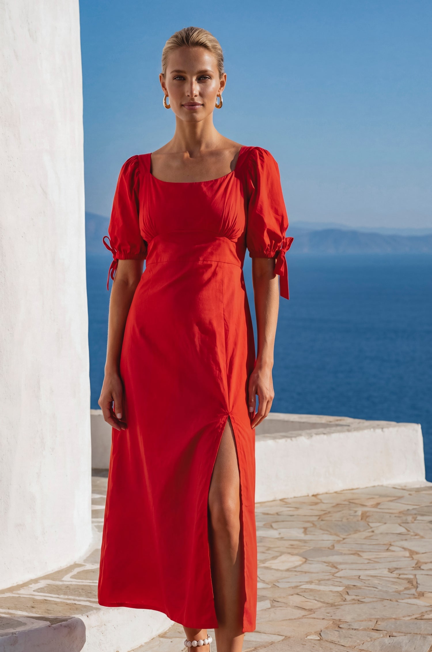 Model wearing the Cala Luna Puff Sleeve Midi Dress in red with a scoop neckline, puff sleeves, and side slit overlooking the sea.