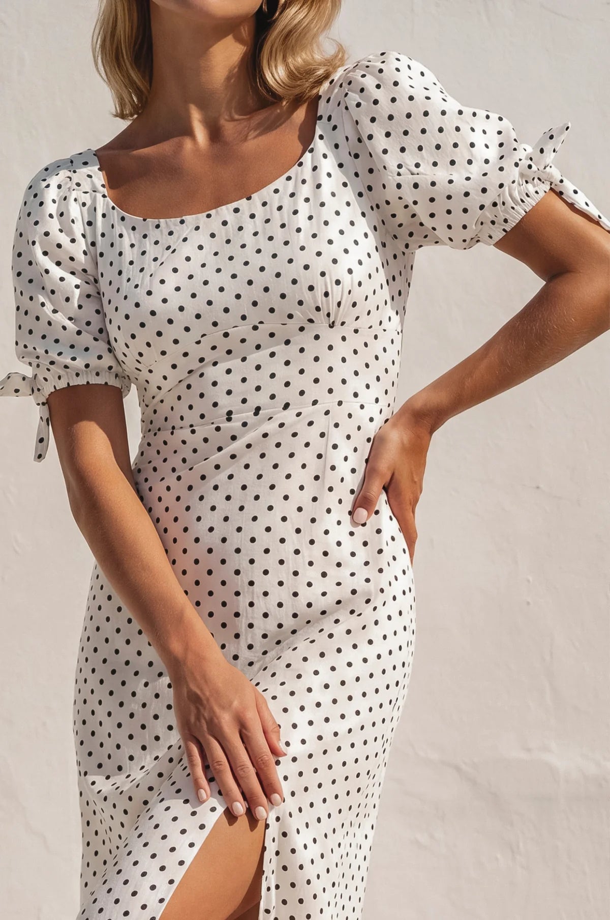 Close up of the Cala Luna Puff Sleeve Midi Dress in white polka dot highlighting the scoop neckline, fitted bodice, puff sleeves, and side slit.