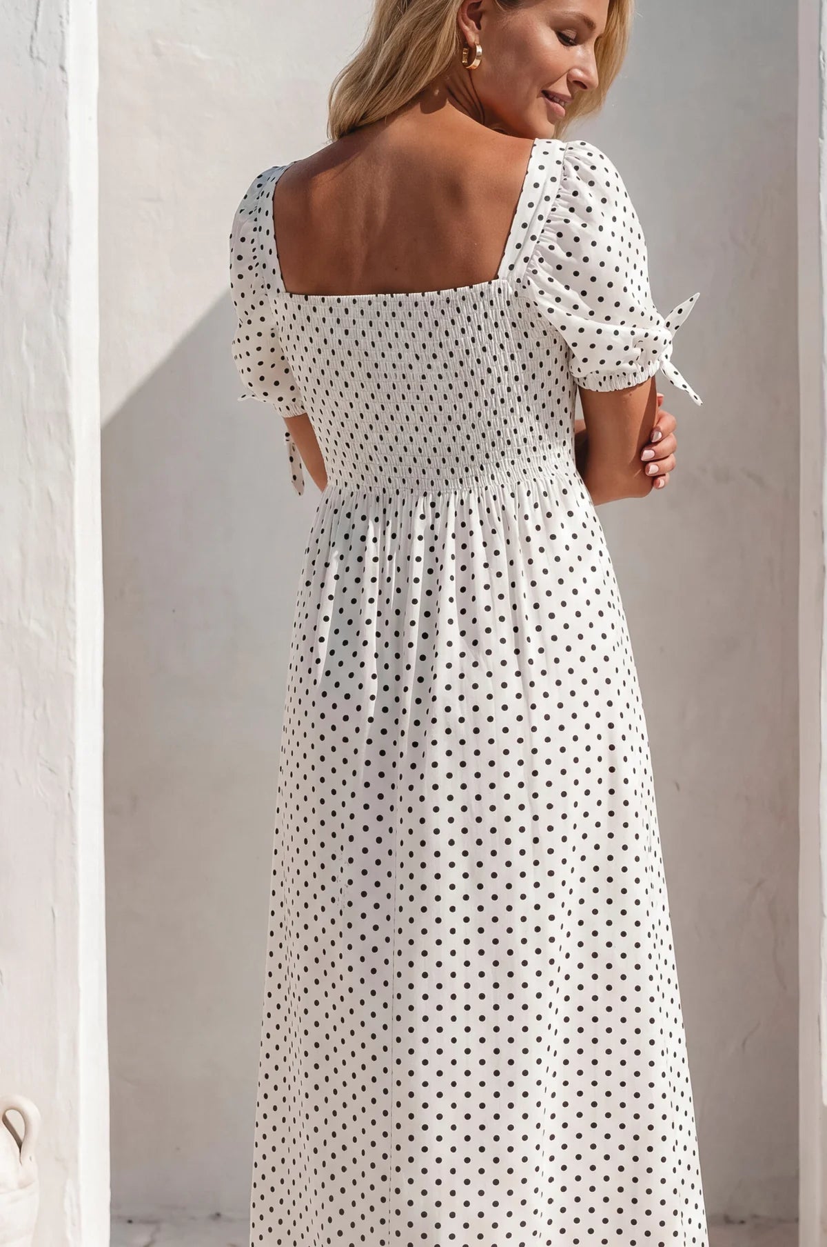 Back view of the Cala Luna Puff Sleeve Midi Dress in white polka dot featuring the smocked back and puff sleeves with tie details.