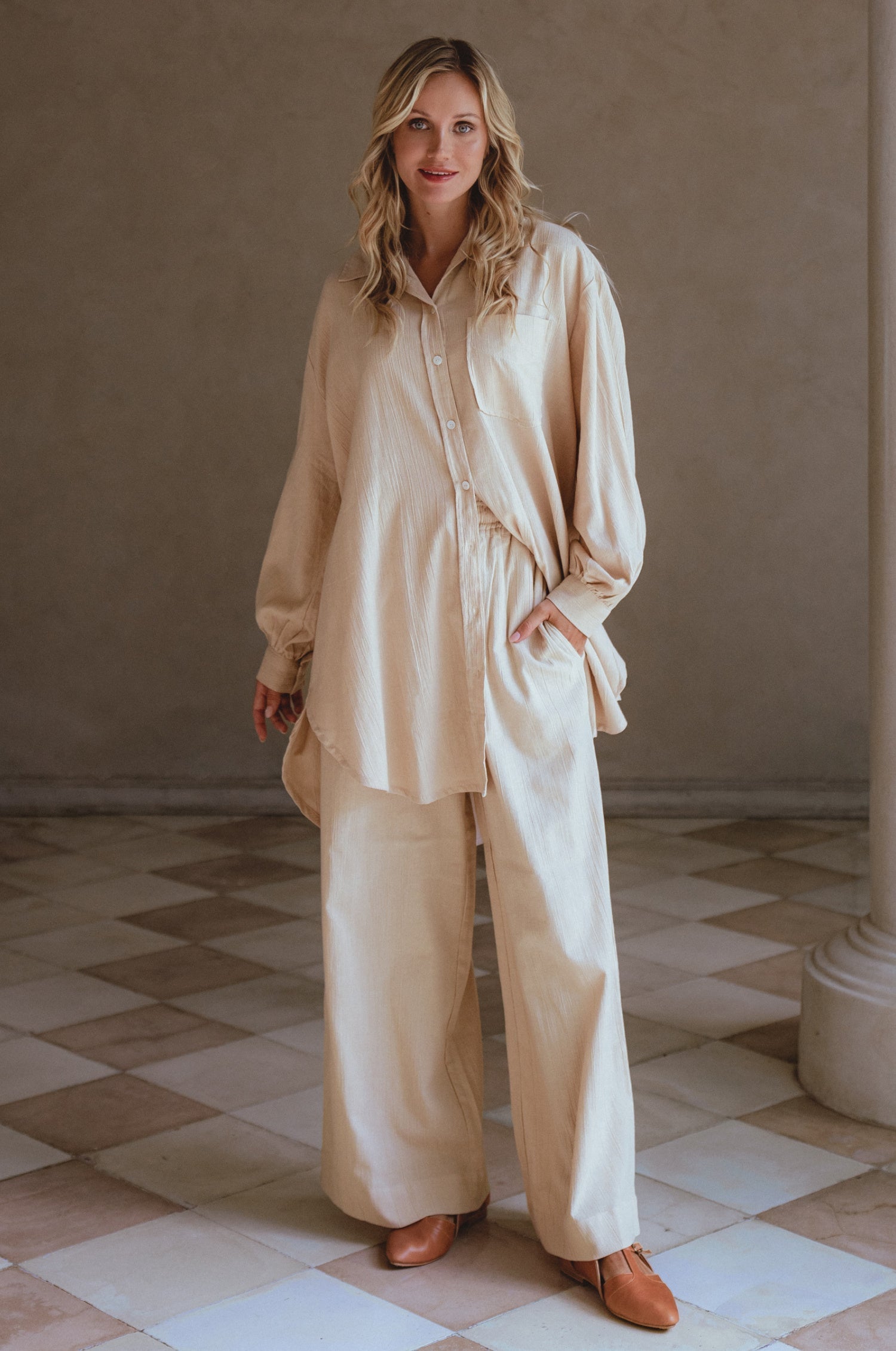 Woman wearing a beige matching set in a room with tiled floor and neutral walls.