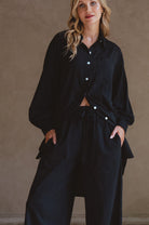 Woman wearing a black outfit with white buttons against a beige background