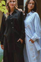 Two women wearing long shirts, one black and one white, standing close together.