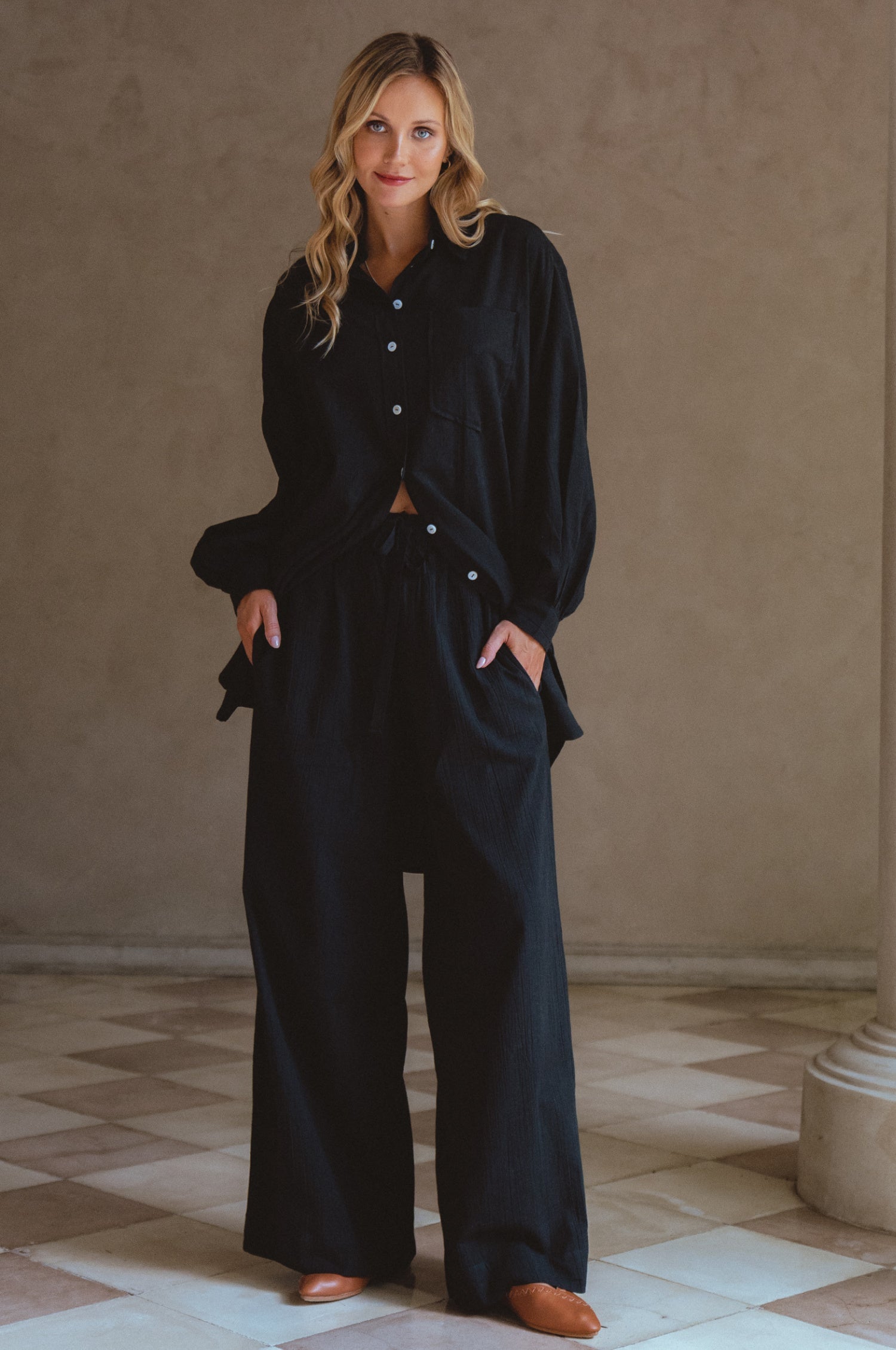 Woman wearing a black outfit standing in a room with a beige wall and tiled floor.
