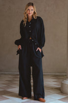 Woman wearing a black outfit standing in a room with a beige wall and tiled floor.