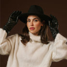 Woman wearing a black hat, white sweater, and black gloves against a dark background