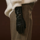 Black leather glove on a person wearing brown pants against a dark background