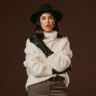 Woman wearing a white fur coat, black hat, and gloves against a brown background