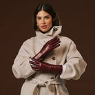 Woman wearing a beige coat and burgundy leather gloves against a brown background