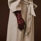 Beige coat with a hand wearing a burgundy leather glove on a brown background