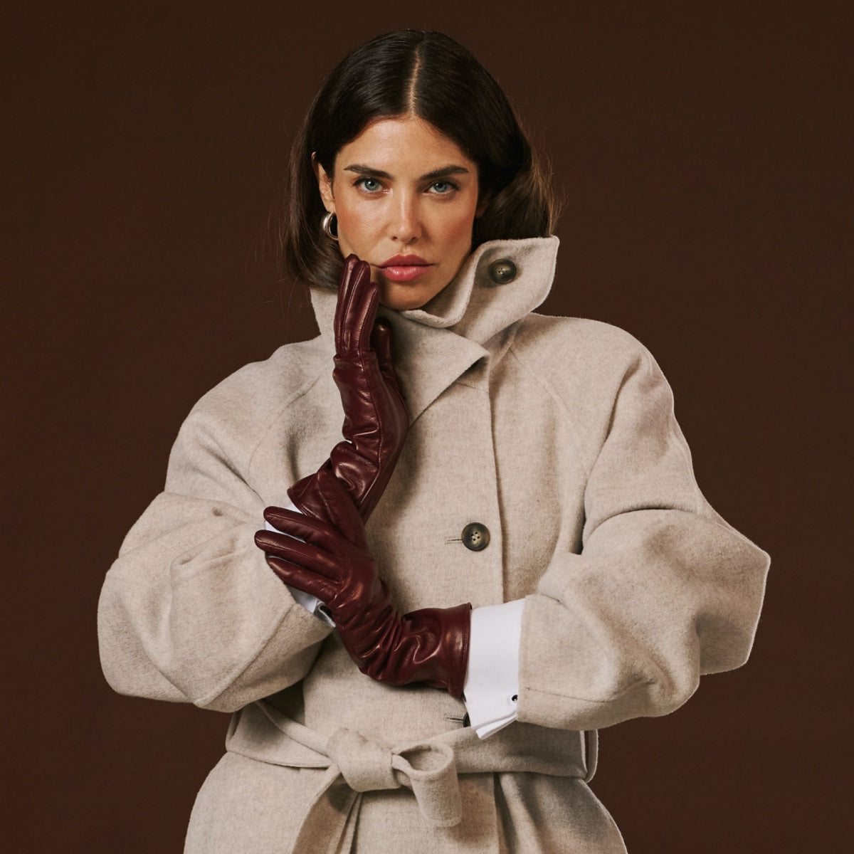 Woman wearing a beige coat and brown gloves against a brown background