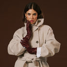 Woman wearing a beige coat and brown gloves against a brown background