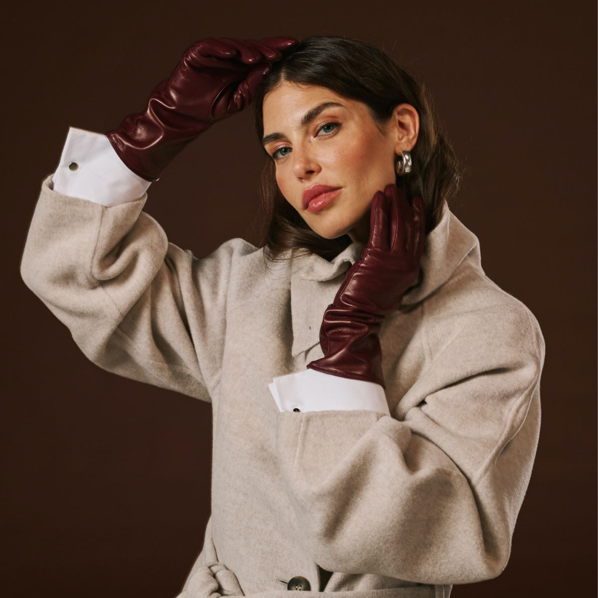 Woman wearing a beige coat and burgundy gloves against a brown background
