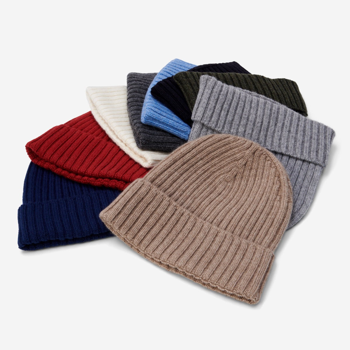 Stack of cashmere knit beanie hats in various colors on a light gray background