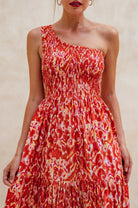 Woman wearing a red and orange patterned one-shoulder maxi dress against a neutral background, front view closeup