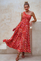 Woman wearing a red floral one-shoulder maxi dress against a beige wall, front vew