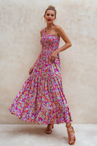 Woman wearing a colorful floral one-shoulder maxi dress against a neutral background