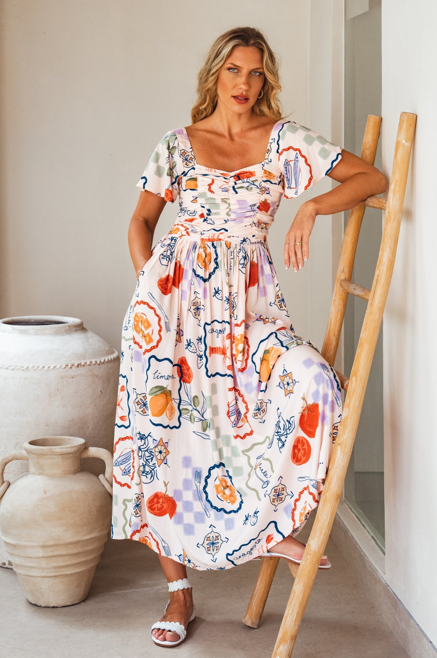 Woman in a colorful floral midi dress standing next to a wooden ladder indoors.