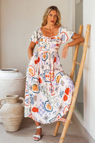 Woman in a colorful floral midi dress standing next to a wooden ladder indoors.
