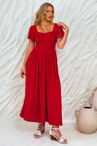 Woman wearing a red midi dress against a textured white wall, front view