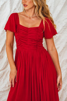 Woman wearing a red dress with a textured white background, closeup of bodice