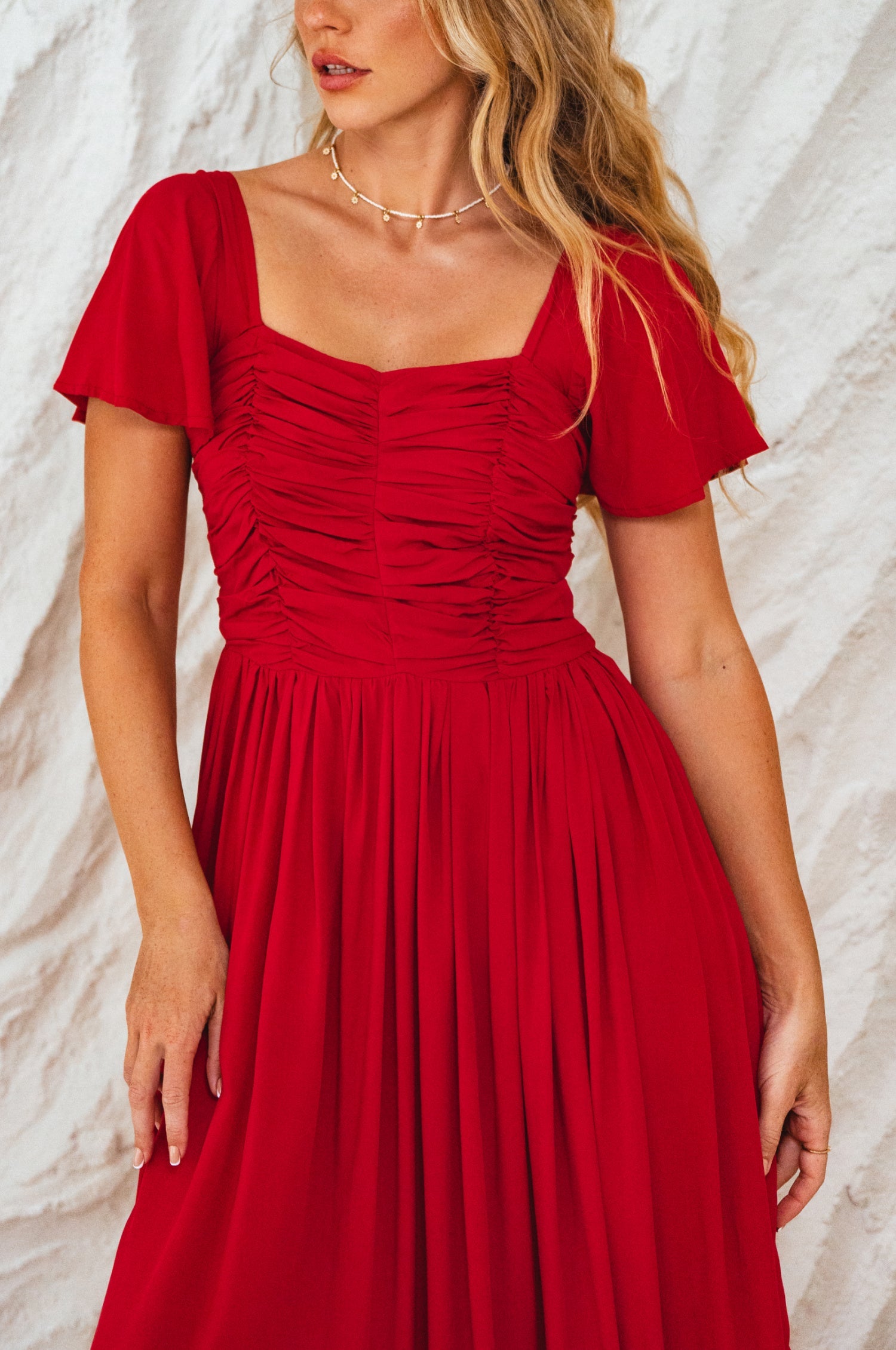 Woman wearing a red dress with a textured white background, closeup of bodice
