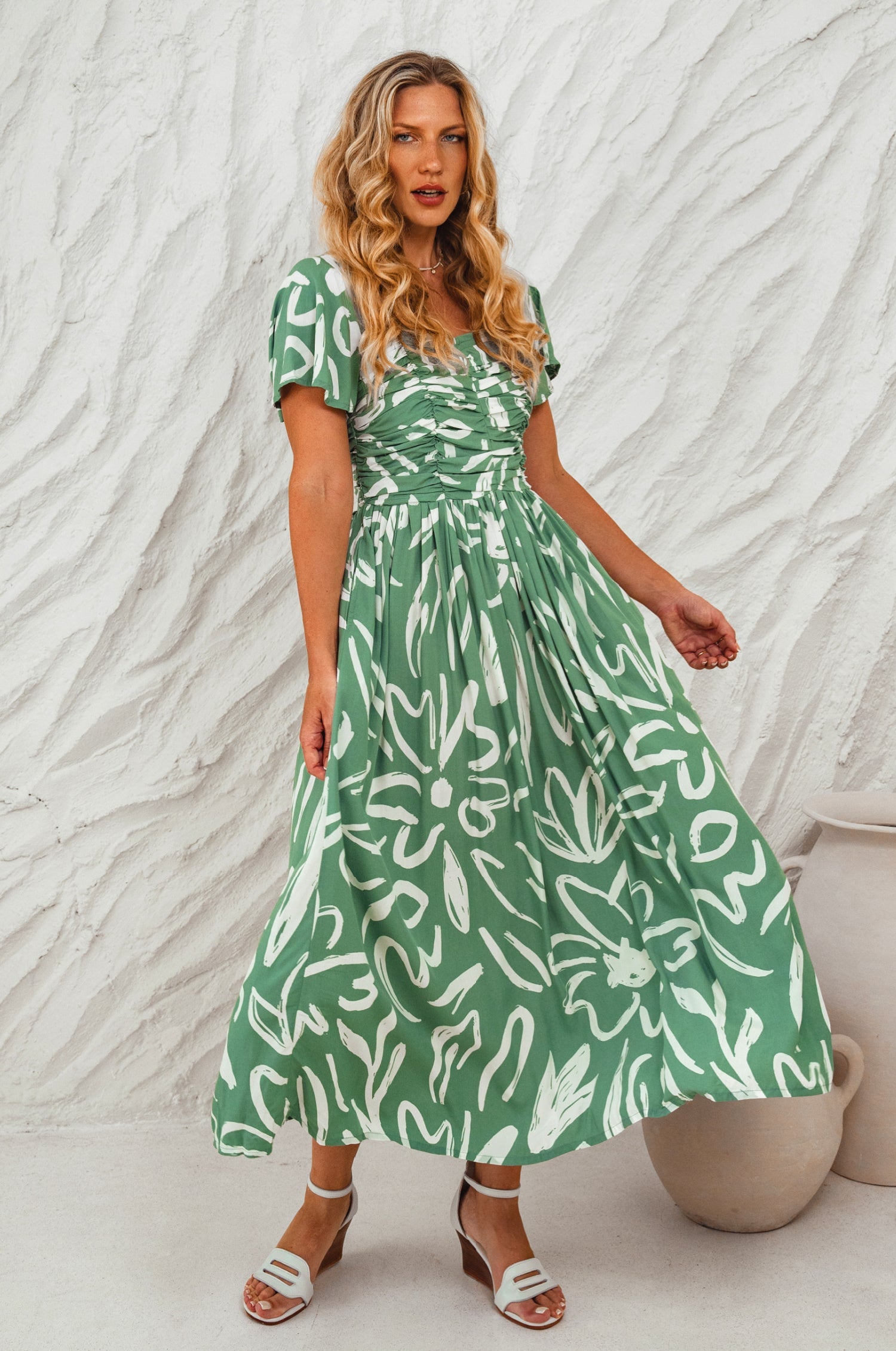 Woman wearing a green floral dress midi against a textured white background, front view
