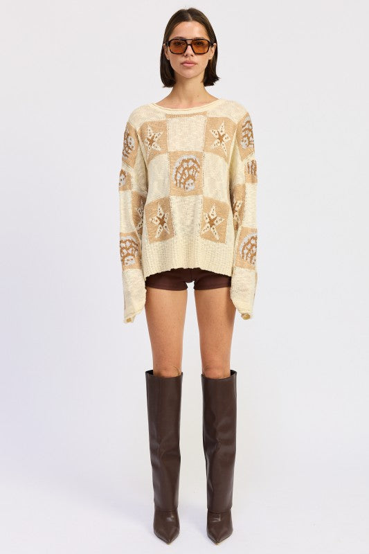 Woman wearing a cream and taupe patchwork knit sweater with star and seashell motifs, front view. and brown knee-high boots on a white background