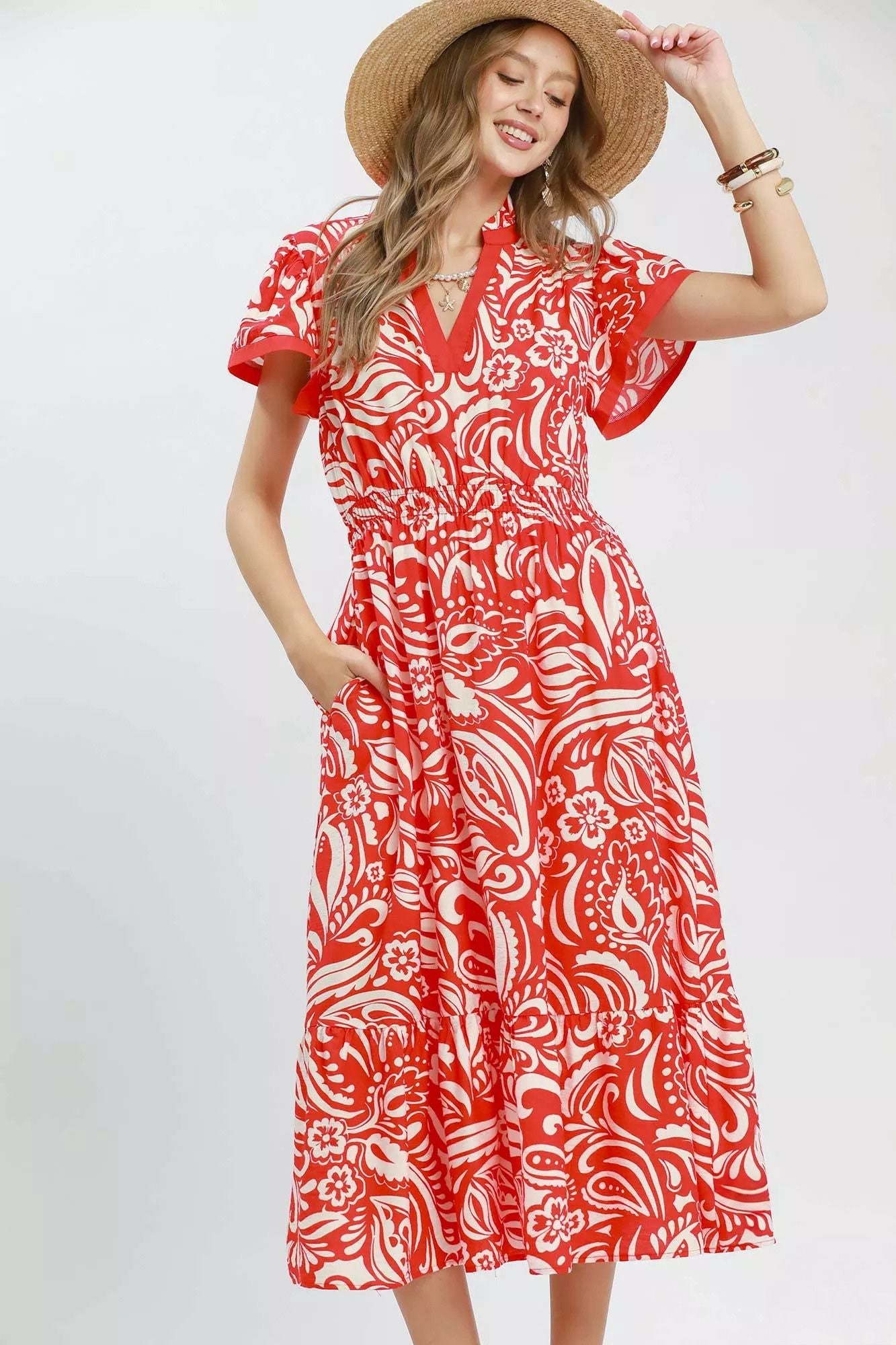Model wearing a red and ivory floral midi dress with flutter sleeves, split neckline, elastic waist, side pockets, and a ruffle hem.