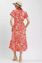 Model wearing a red and ivory floral midi dress with flutter sleeves, split neckline, elastic waist, side pockets, and a ruffle hem.