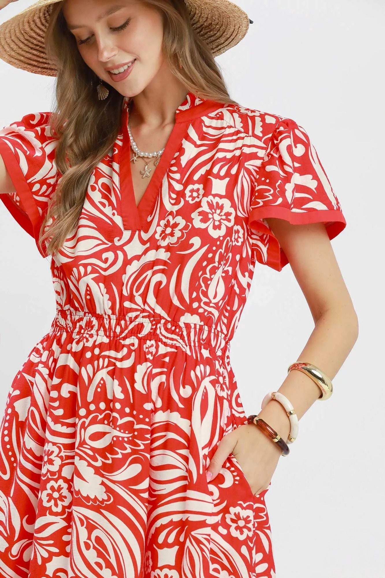 Model wearing a red and ivory floral midi dress with flutter sleeves, split neckline, elastic waist, side pockets, and a ruffle hem.