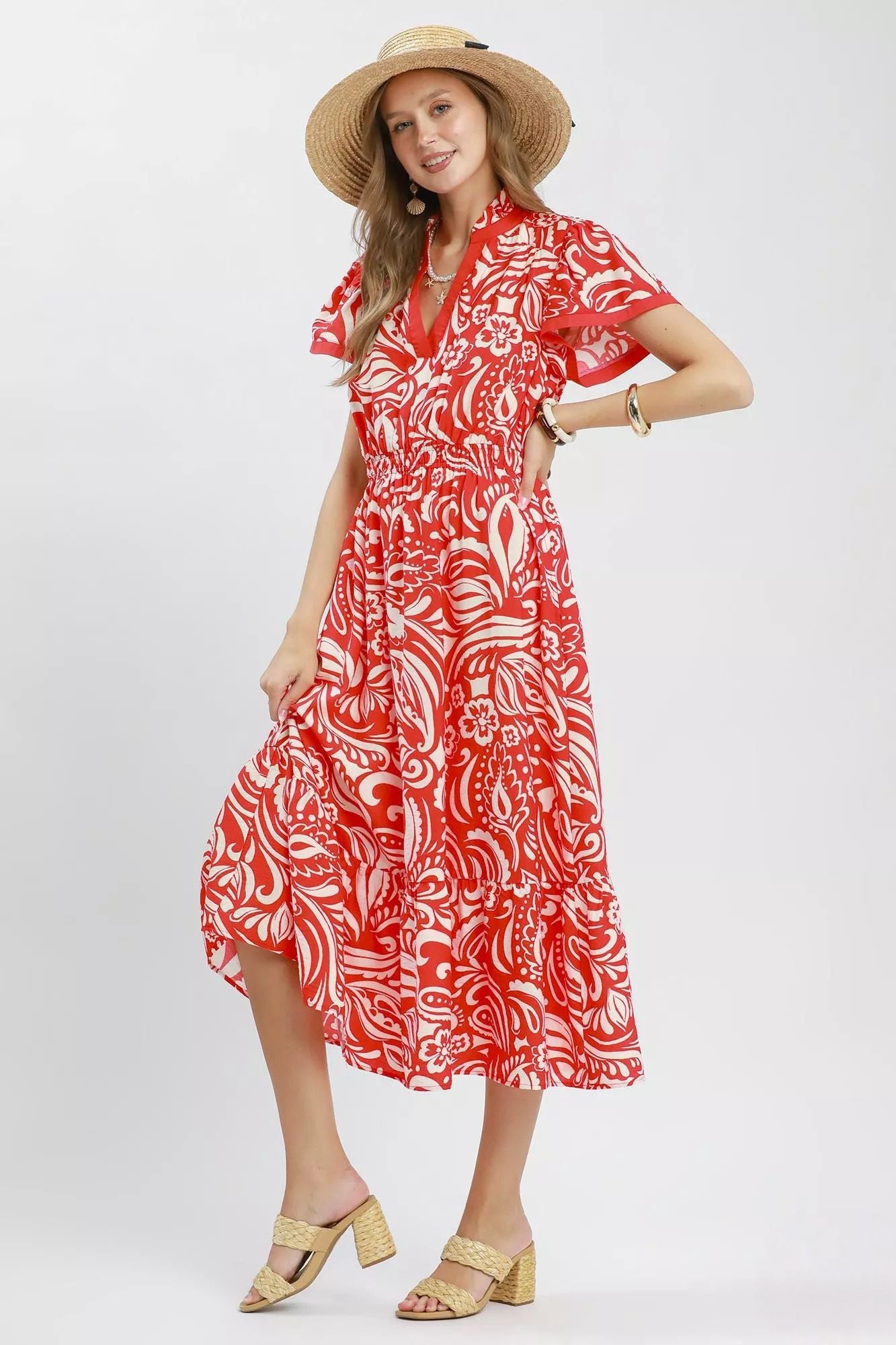 Model wearing a red and ivory floral midi dress with flutter sleeves, split neckline, elastic waist, side pockets, and a ruffle hem.