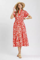 Model wearing a red and ivory floral midi dress with flutter sleeves, split neckline, elastic waist, side pockets, and a ruffle hem.