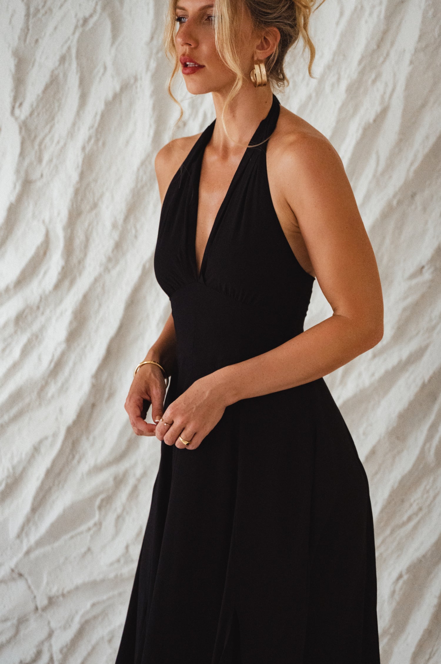 Woman wearing a black soft rayon maxi dress with halter neckline, smocked back, and fitted bodice, on a white background, 3/4 view