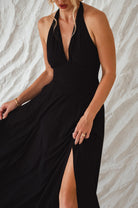 Woman wearing a black soft rayon maxi dress with halter neckline, smocked back, and fitted bodice, on a white background, front close-up view of bodice and slit