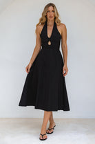 Woman wearing a sleeveless black cotton midi dress with halter neckline against a white background