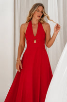 Woman wearing a sleeveless red cotton midi dress with halter neckline against a white curtain background