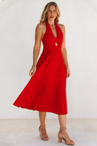 Woman wearing a sleeveless red cotton midi dress with halter neckline with a white background